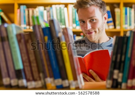 Portrait of a young male student reading a book amid bookshelves in the college library