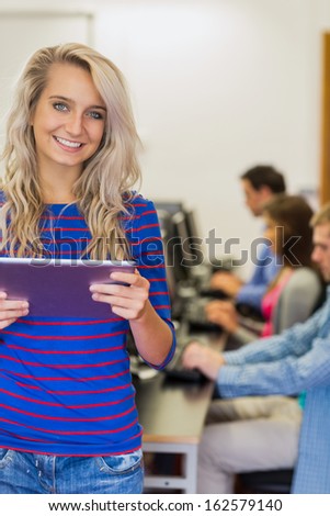 Teacher holding tablet PC with young college students using computers in the computer room