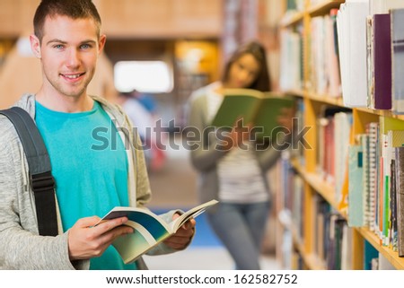 Portrait of two young students reading by bookshelf in the library