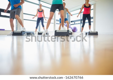 Low section of instructor with fitness class performing step aerobics exercise in gym