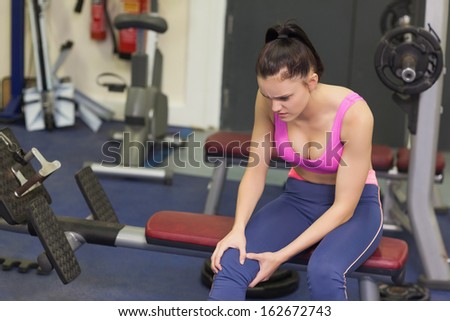 Healthy young woman with an injured knee sitting in the gym