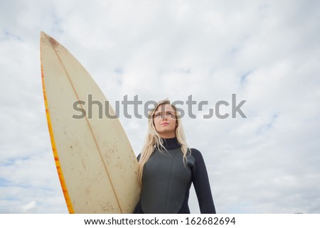 Low angle view of a beautiful young woman with surfboard against cloudy sky