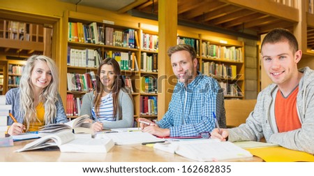 Group portrait of four students writing notes at desk in the college library