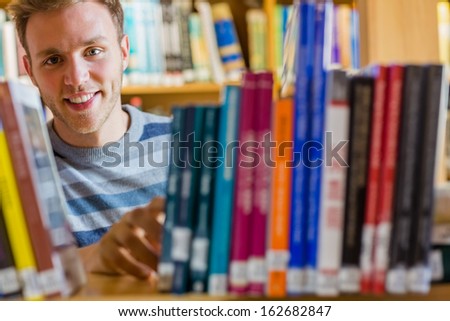 Close up portrait of a young male student selecting book from bookshelf in the college library