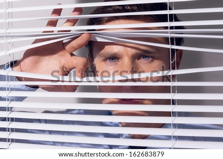 Close up portrait of a young businessman peeking through blinds