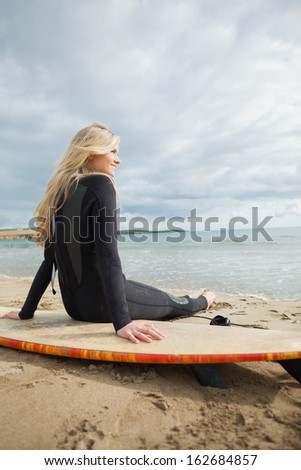 Rear view of a smiling beautiful blond in wet suit with surfboard at the beach