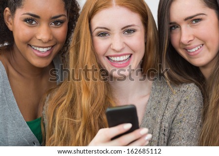 Close up portrait of cheerful young female friends with mobile phone together at home