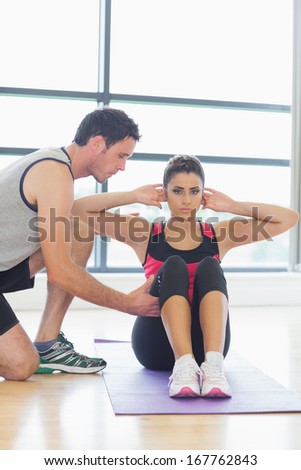 Male trainer assisting young woman with pilate exercises in the fitness studio
