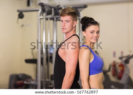 Side view portrait of a sporty young woman and man standing back to back in the gym