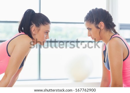 Close-up side view of two angry young women staring at each other at a bright gym