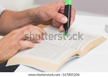 Close-up of a man\'s hands highlighting text in book on the table