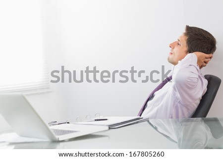 Side view of a relaxed businessman sitting with hands behind head in the office