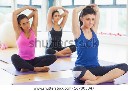 Class stretching hands behind heads on mats at yoga class in fitness studio