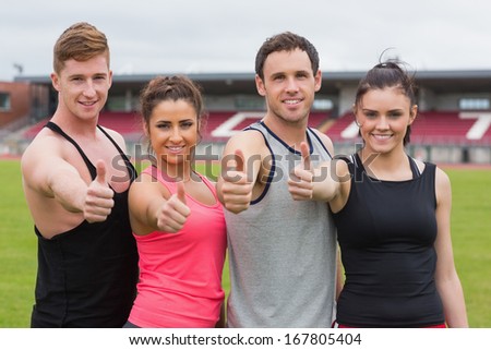 Portrait of happy fit young people gesturing thumbs up on ground against the stadium