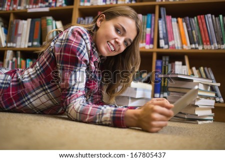 Smiling student lying on library floor using tablet pc in college