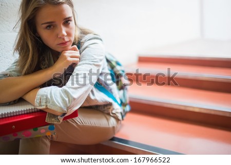 Sad lonely student sitting on stairs looking at camera in college