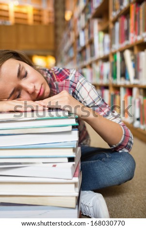 Dozing young student sitting on library floor leaning on pile of books in college
