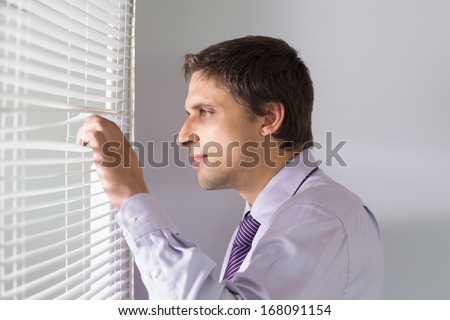 Side view of a young businessman peeking through blinds in the office
