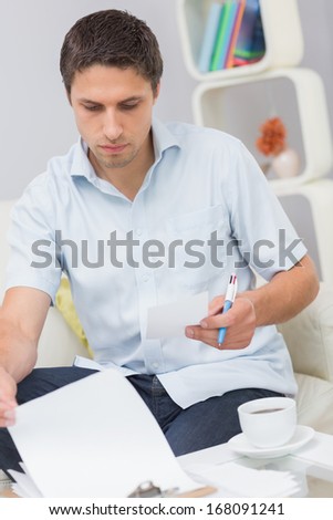 Worried young man sitting on couch and paying his bills in the living room at home