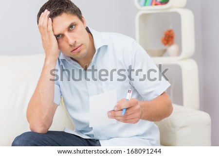 Portrait of a worried young man paying his bills in the living room at home