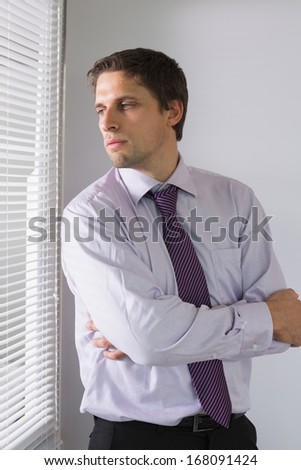 Serious young businessman peeking through blinds in the office
