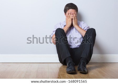 Full length of a young businessman sitting on floor with hands covering face in an empty room