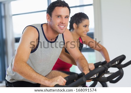 Portrait of a young man and woman working out at exercise bike class in gym