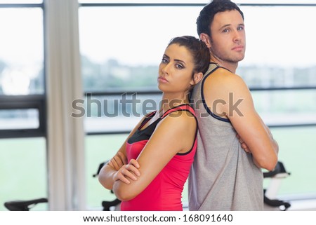 Side view portrait of a serious young woman and man standing back to back in a bright gym