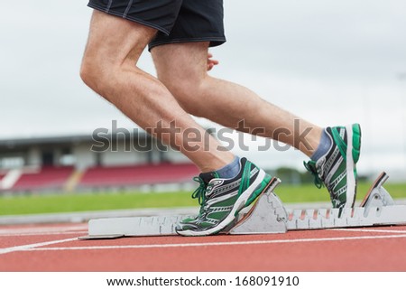 Side view low section of a young man ready to race on running track