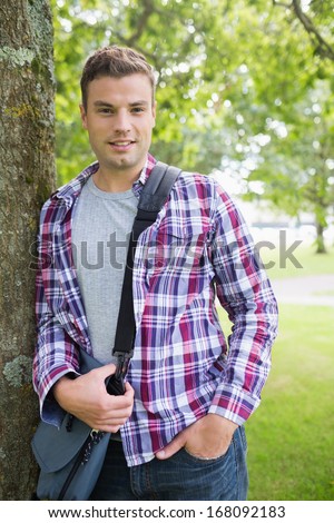 Handsome student leaning on tree looking at camera on college campus
