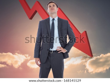Serious businessman with hand on hip against red arrow pointing down against sky