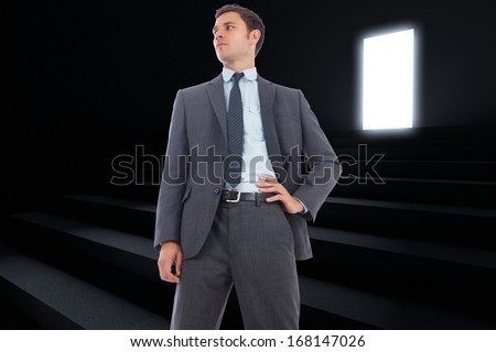 Stern businessman with hand on hip against steps leading to light in the darkness