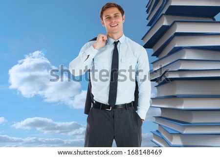Smiling businessman holding his jacket against pile of books against sky