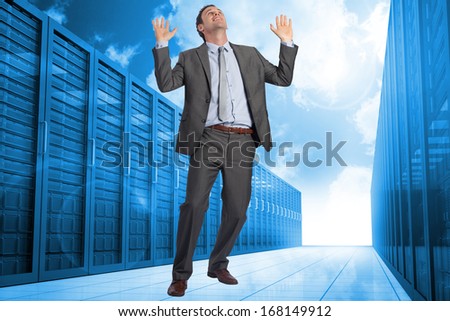 Businessman posing with arms raised against server hallway in the blue sky