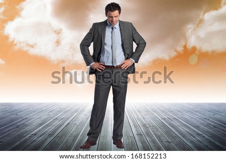 Smiling businessman with hands on hips against cloudy sky background