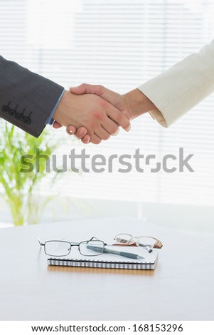 Close-up of shaking hands over eye glasses and diary after a business meeting at office desk