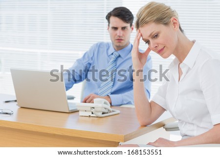 Upset young businesswoman with man working on laptop at office desk