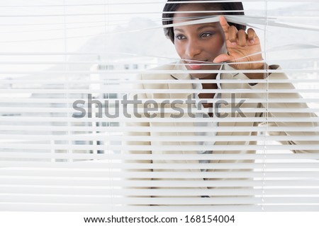 Portrait of a young businesswoman peeking through blinds in office