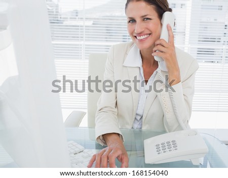 Smiling young businesswoman using computer and phone at office desk