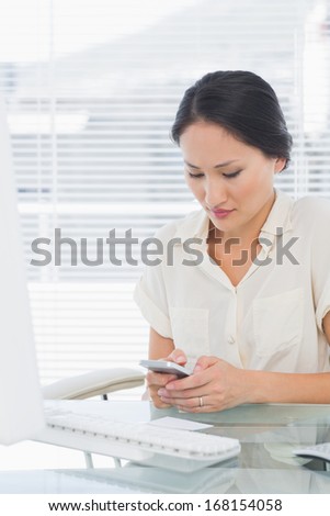 Concentrated young businesswoman text messaging in front of computer at office desk