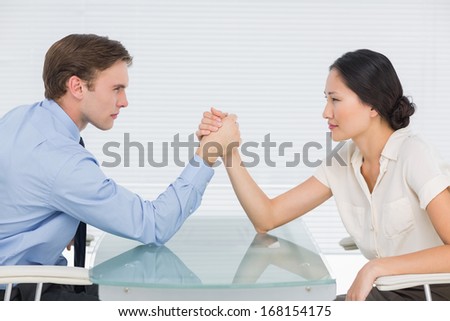 Side view of serious young business couple arm wrestling at office desk