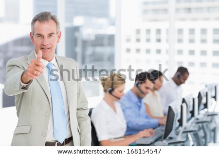 Happy businessman gesturing thumbs up with executives using computers in the office