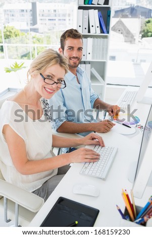 Side view of smiling casual young couple working on computers in a bright office