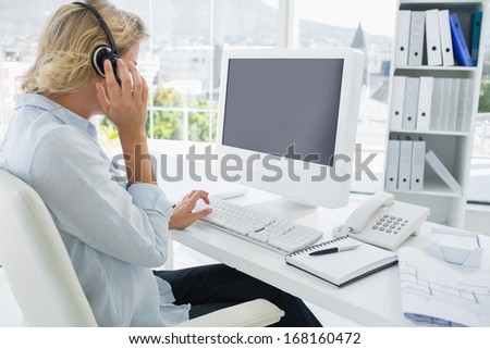 Side view of a casual young woman with headset using computer in a bright office