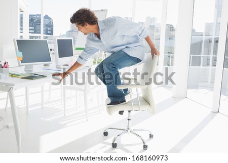 Full length of a young man standing over chair in a bright office