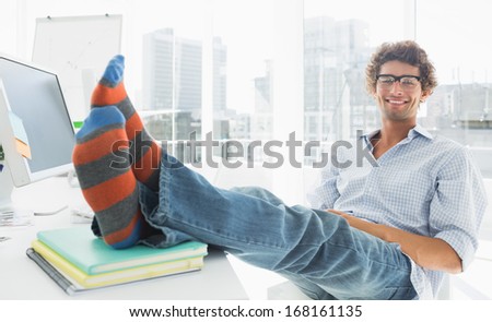 Portrait of a relaxed casual young business man with legs on desk in a bright office