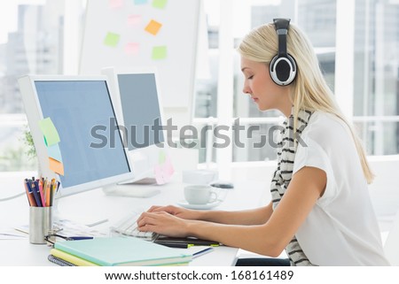 Side view of a casual young woman with headset using computer in a bright office