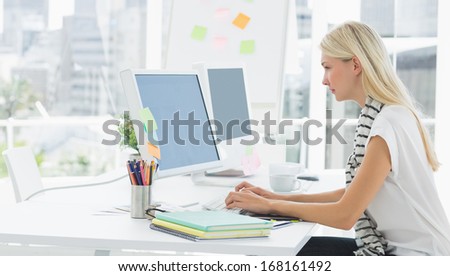 Side view of a casual young woman using computer in a bright office