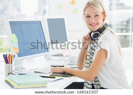 Side view of a casual young woman with headset at computer desk in a bright office