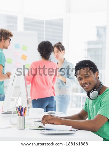 Side view portrait of a casual man using computer with group of colleagues behind in a bright office